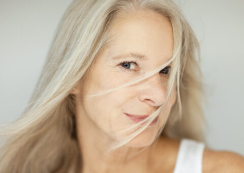 older white women looking at camera with hair in her face with gray background