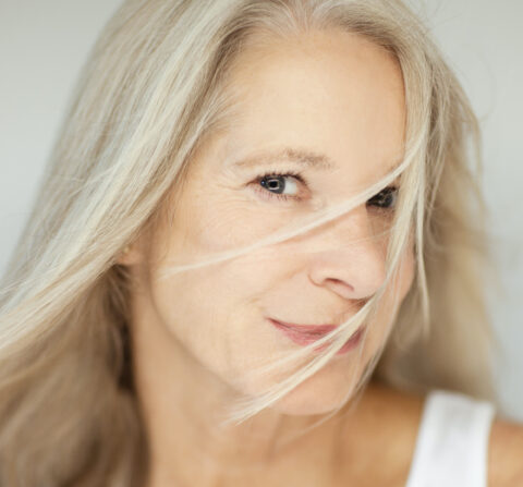 older white women looking at camera with hair in her face with gray background