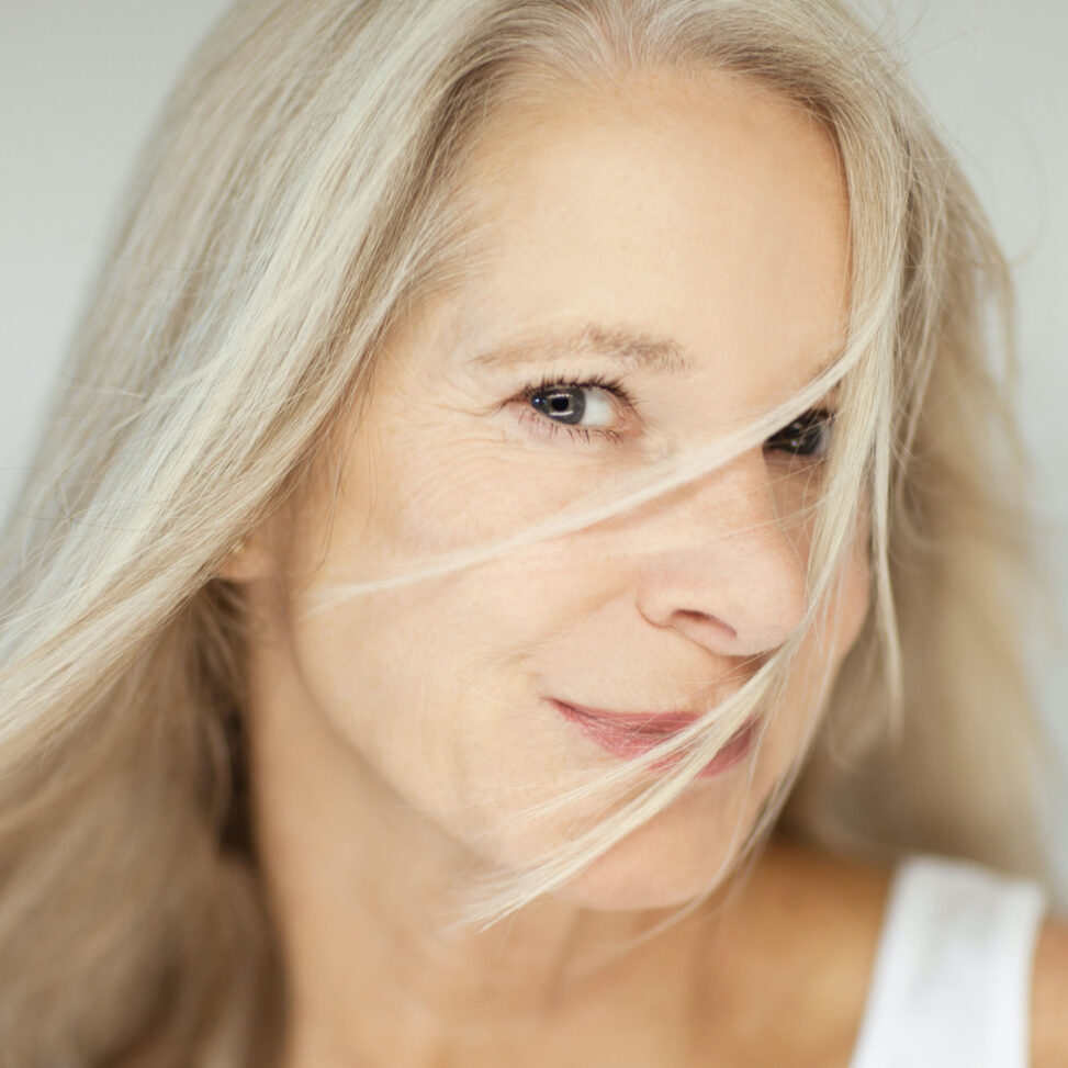 older white women looking at camera with hair in her face with gray background