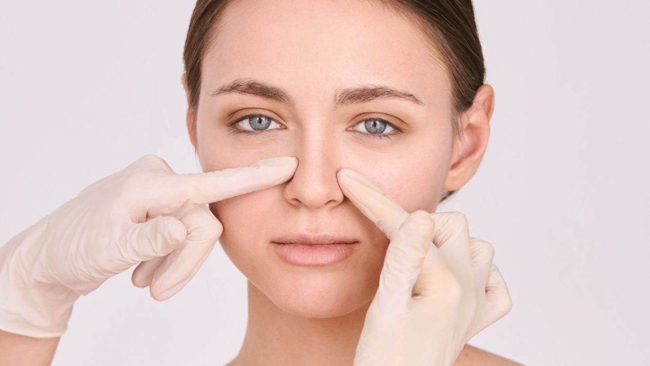 Medical provider in gloves examining woman's nose during non-surgical rhinoplasty consultation