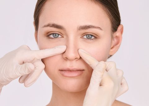Medical provider in gloves examining woman's nose during non-surgical rhinoplasty consultation