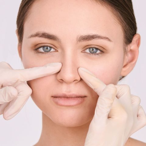 Medical provider in gloves examining woman's nose during non-surgical rhinoplasty consultation