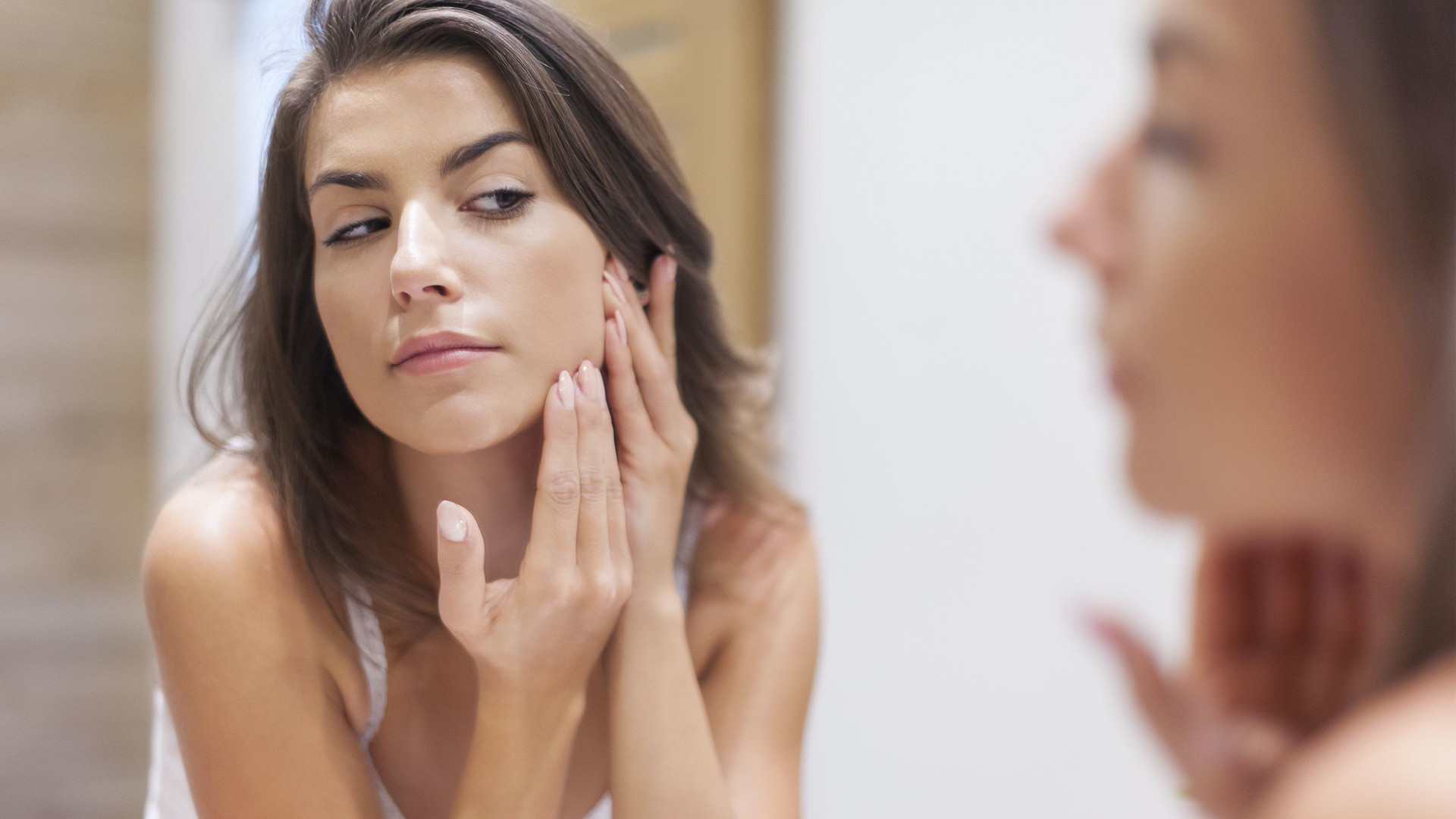 woman putting facial product on her face in the mirror