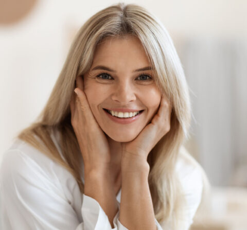 older white women smiling at camera with her hands on her cheeks in a living room