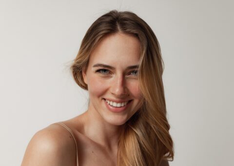 Smiling woman with smooth, youthful skin posing against a neutral background, representing natural results after a professional skin-tightening treatment.