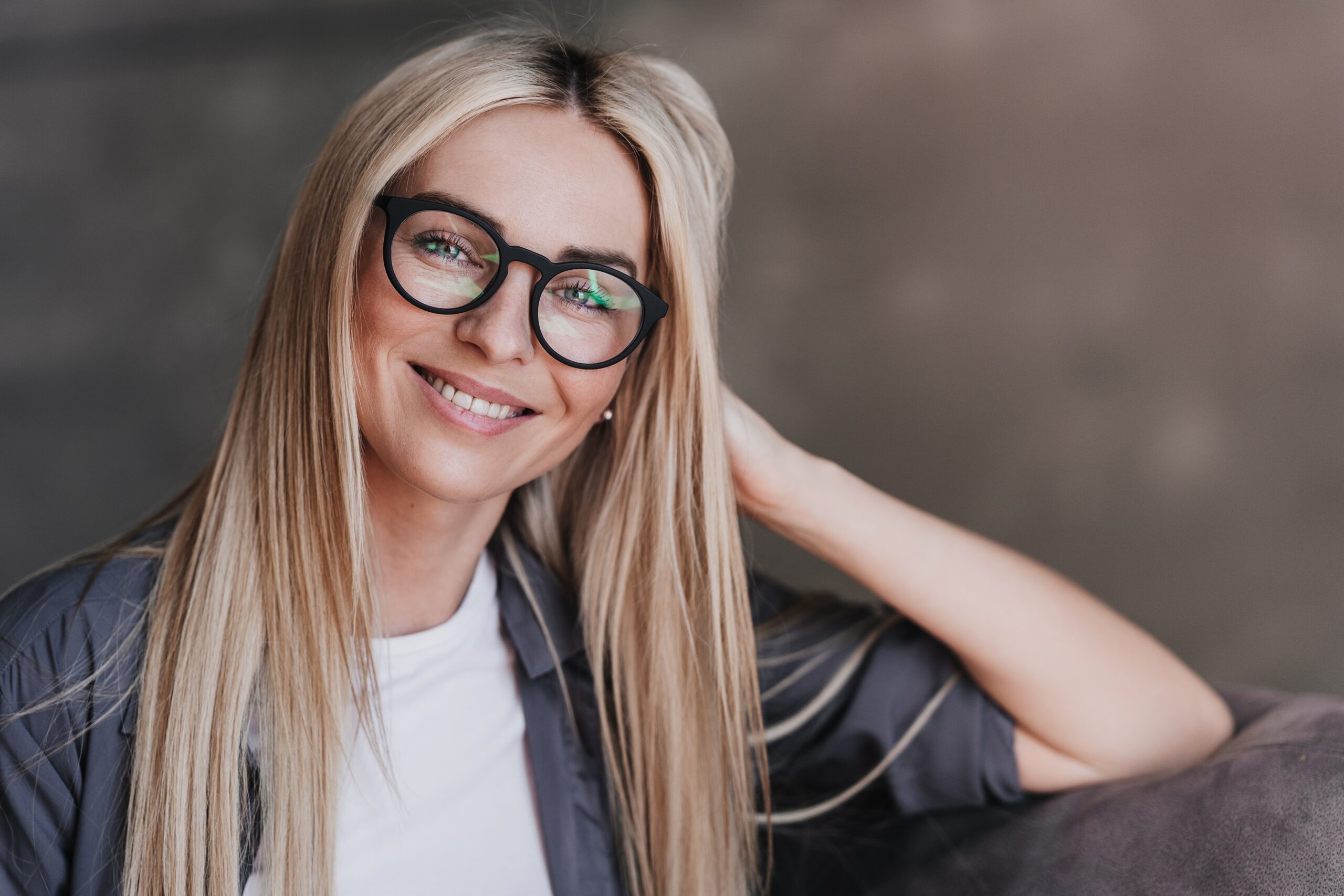 woman wearing glasses smiling at the camera while leaning on her hand.