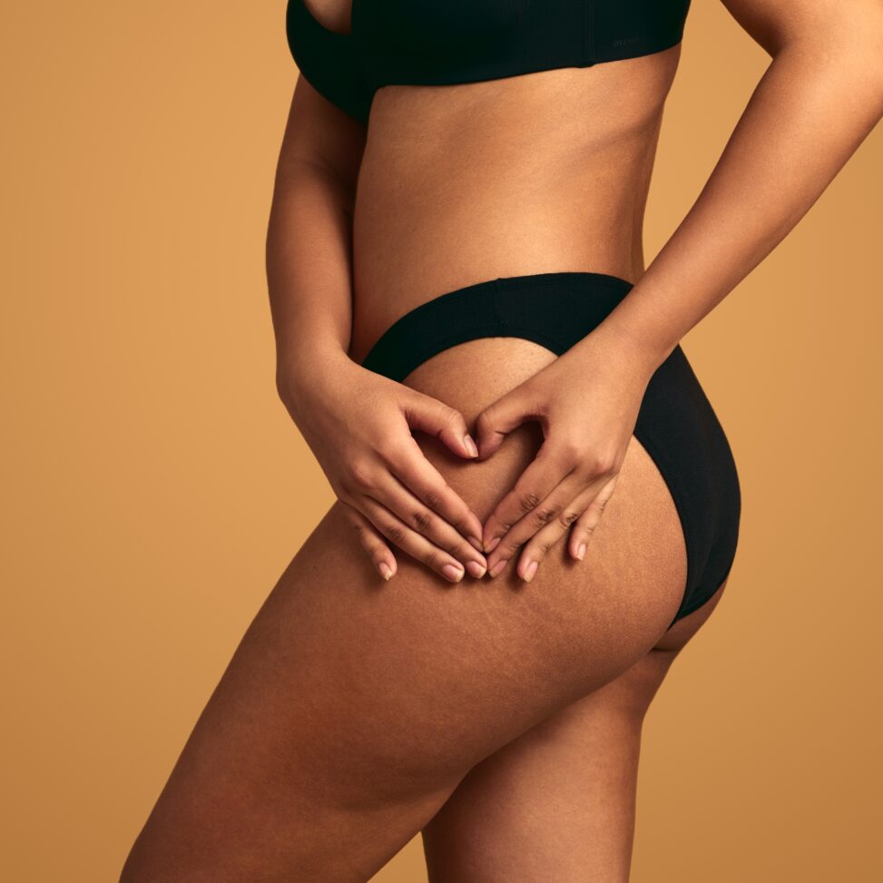 african american women touching her upper thigh with a tan background