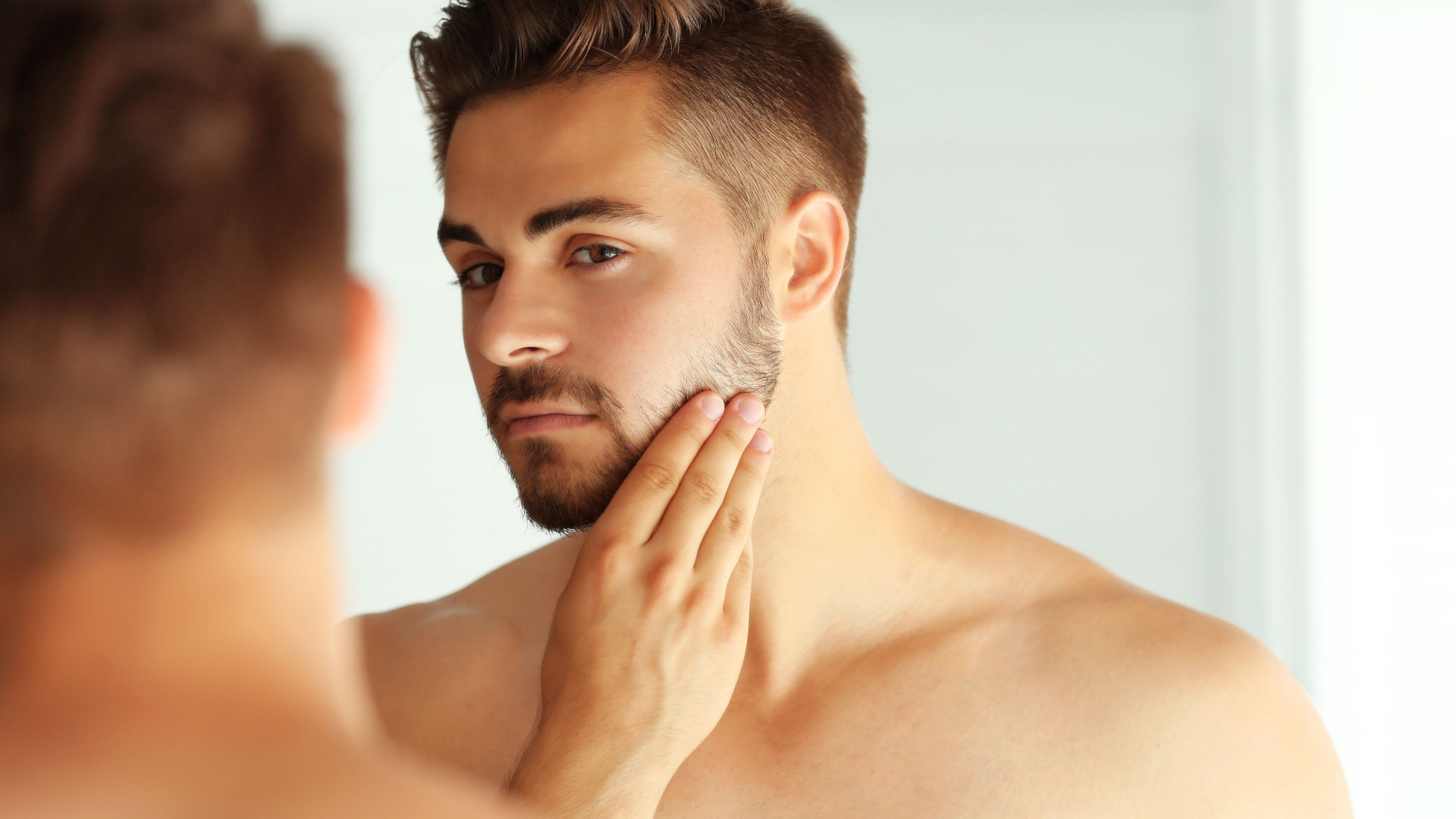 man looking at his chin in the mirror