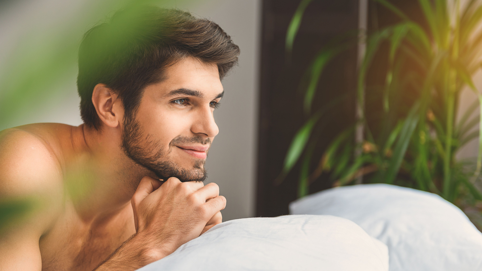 handsome man looking off to the side while on a white couch and shirtless