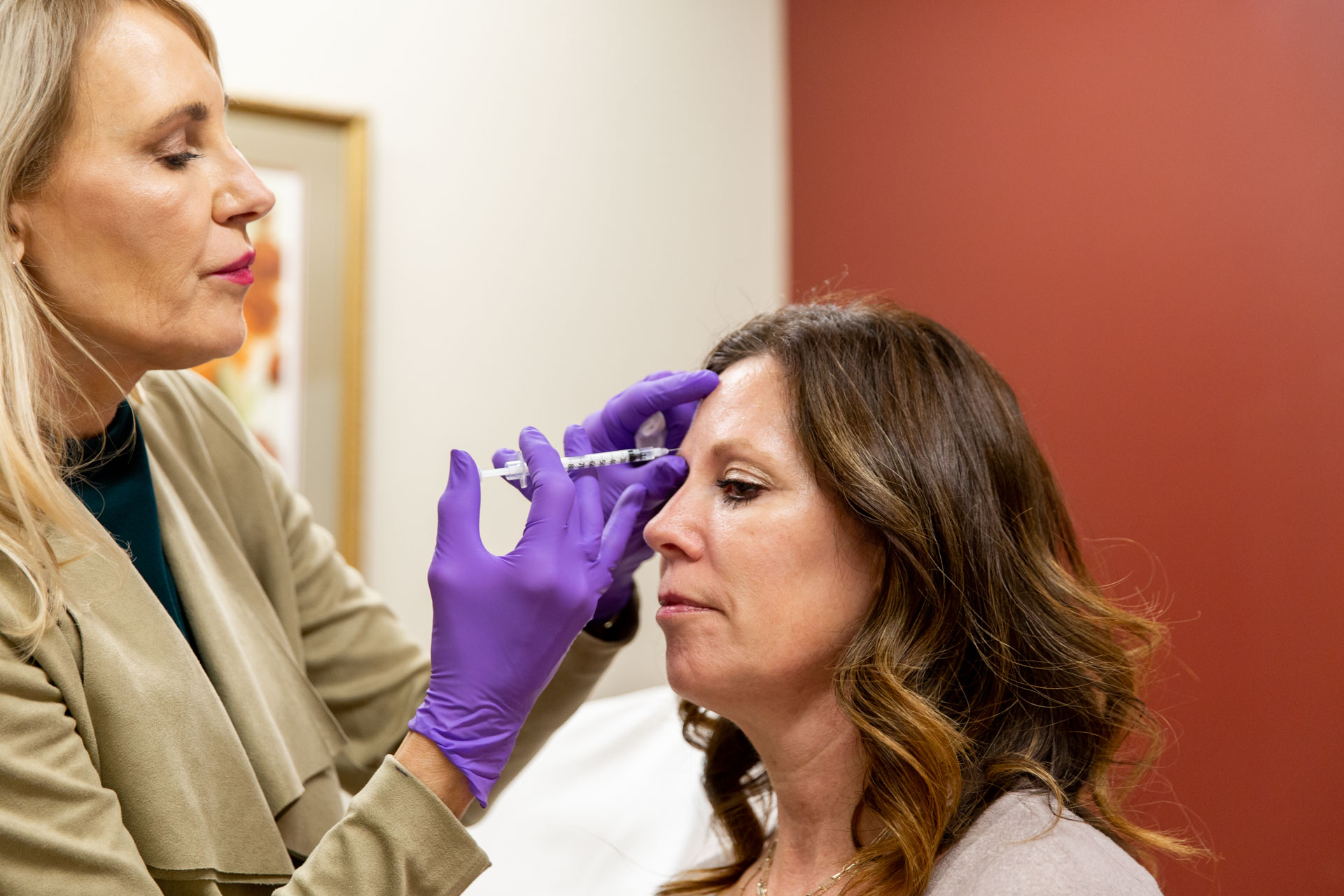 A medical professional wearing purple gloves administers a Botox or Dysport injection to a woman’s forehead in a clinical setting, demonstrating a wrinkle-relaxing treatment.