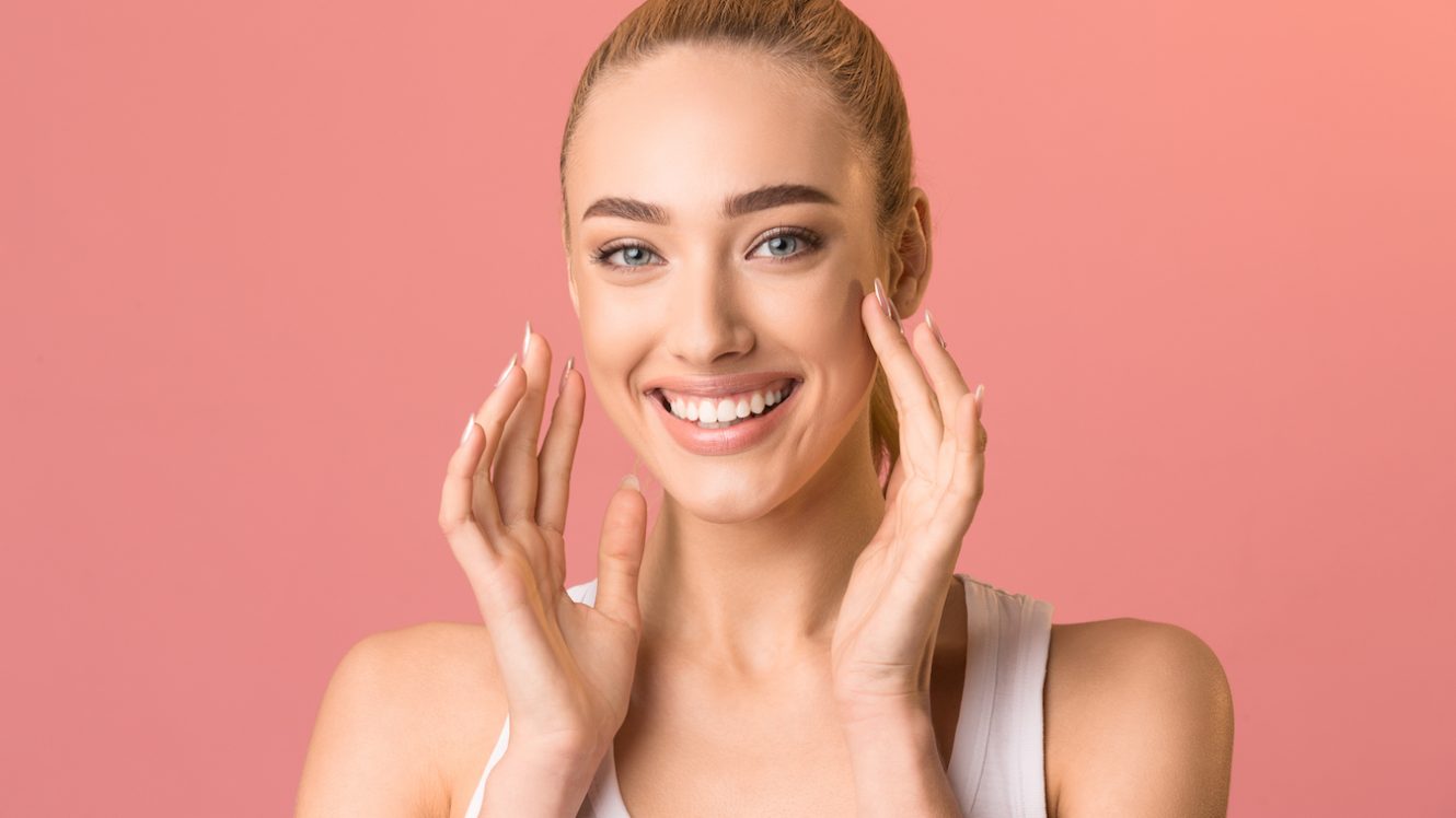 Cheerful Girl Touching Face Smiling To Camera, Pink Studio Background