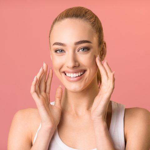 Cheerful Girl Touching Face Smiling To Camera, Pink Studio Background