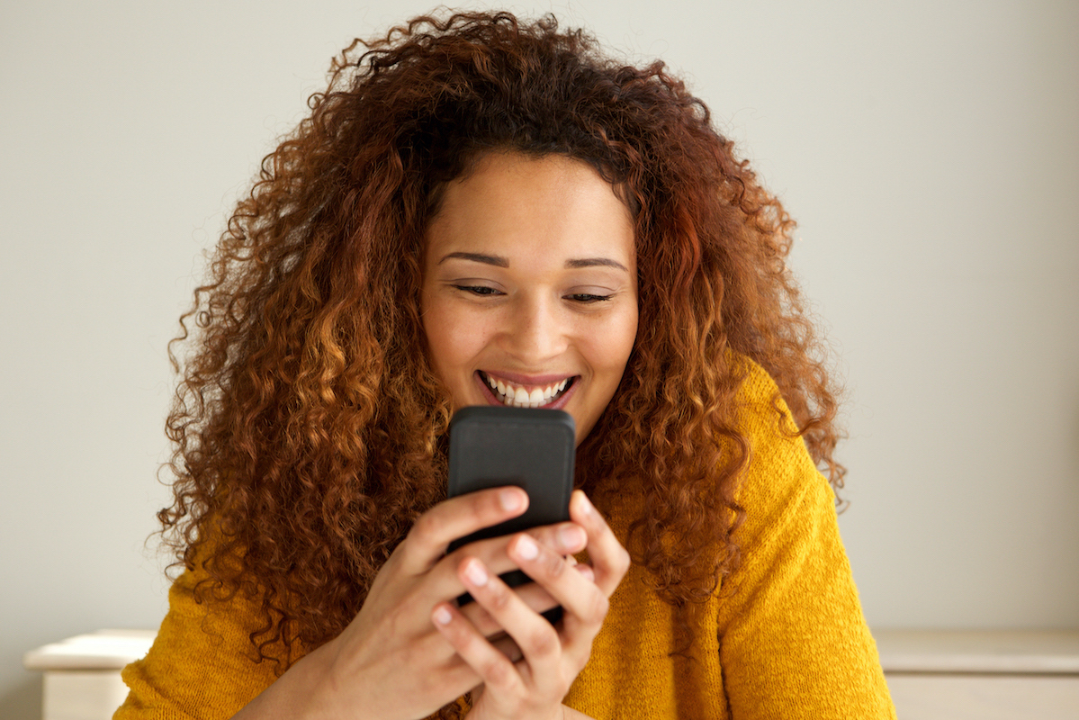 Close up cool young woman smiling and looking at cellphone