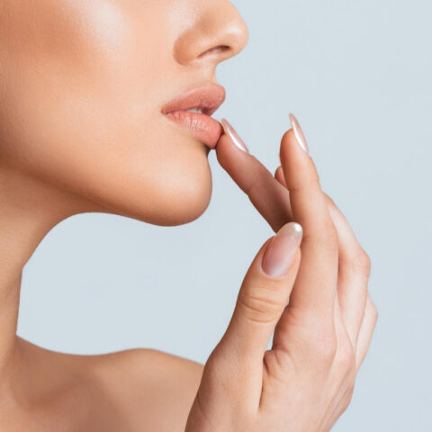 A woman with light skin is captured in profile her left hand gently touching her lower lip with her finger