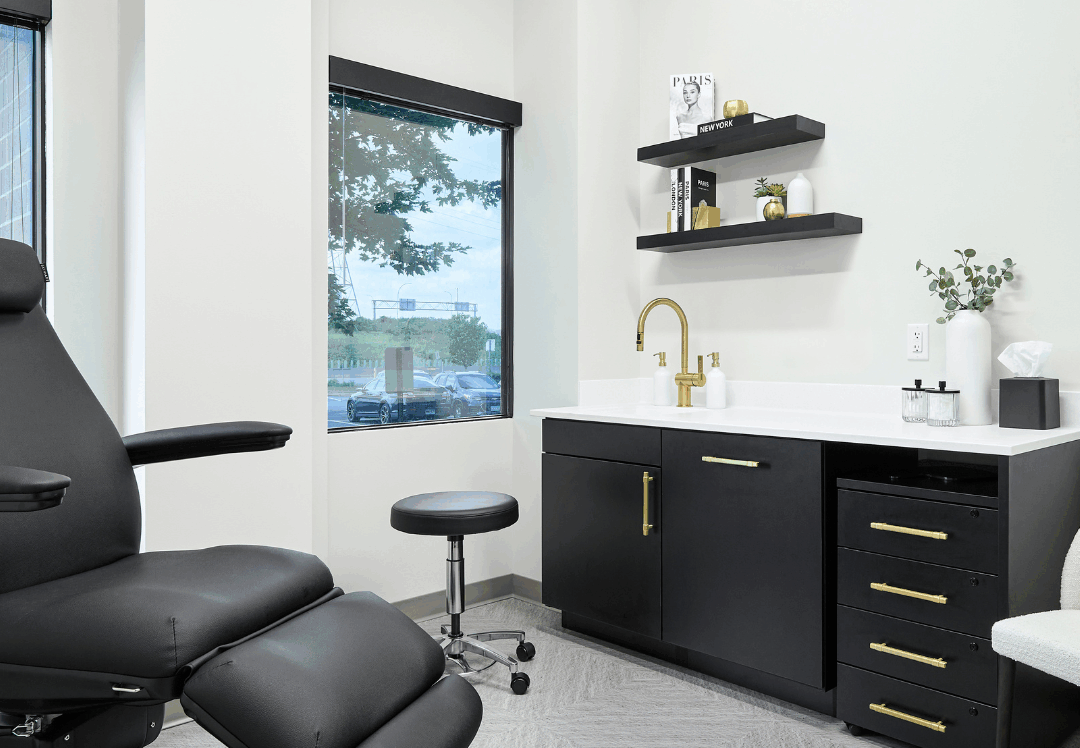 Primary Alt Text Option Modern aesthetic clinic treatment room with black reclining exam chair, sleek cabinetry, and minimalist decor