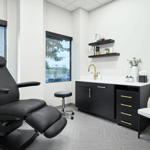 Primary Alt Text Option Modern aesthetic clinic treatment room with black reclining exam chair, sleek cabinetry, and minimalist decor