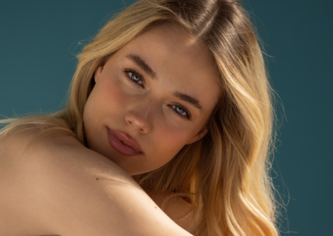 Close-up of a woman with long blonde hair and clear, smooth skin resting her shoulder forward, highlighting natural glow and youthful skin textu