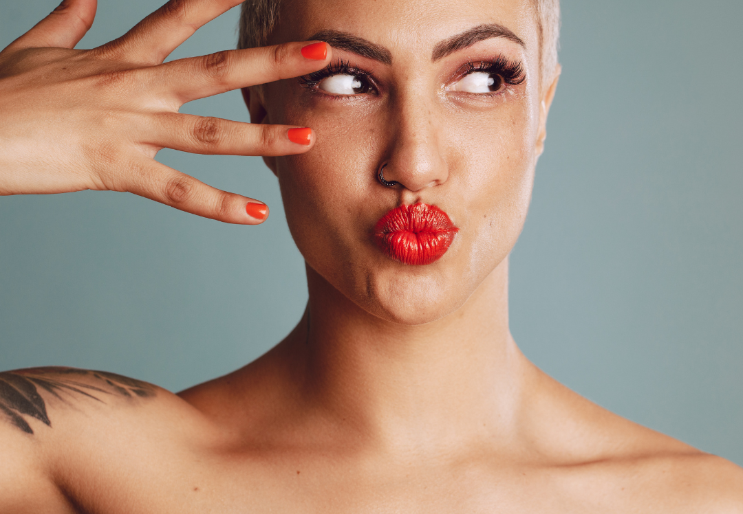 Portrait of a woman with short blonde hair and bright red lipstick posing playfully with her hand near her face, highlighting smooth, youthful skin and facial definition.