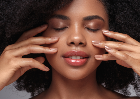 Close-up of a woman with natural curly hair gently touching her face, eyes closed, highlighting smooth skin, softness, and a calm, refreshed appearance.