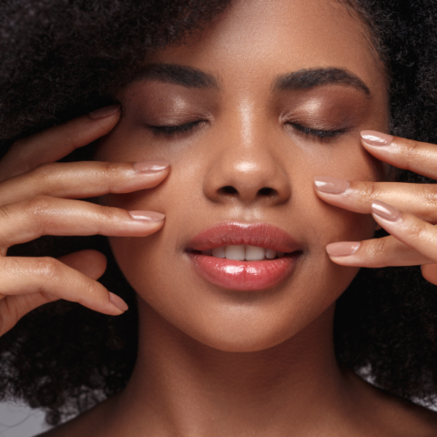 Close-up of a woman with natural curly hair gently touching her face, eyes closed, highlighting smooth skin, softness, and a calm, refreshed appearance.