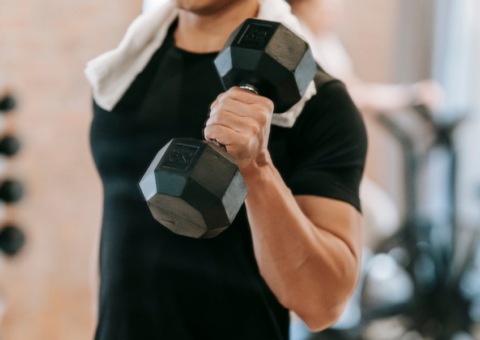 Man in a black athletic shirt lifting a dumbbell during a strength training workout at the gym.