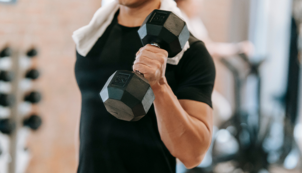 Man in a black athletic shirt lifting a dumbbell during a strength training workout at the gym.